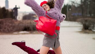 A fashionable young woman jumping with joy outdoors, wearing vibrant clothing and accessories.